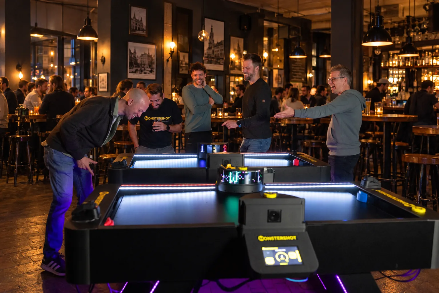 Fünf Männer spielen und jubeln an zwei Monstershot®-Spieltischen in einer Bar